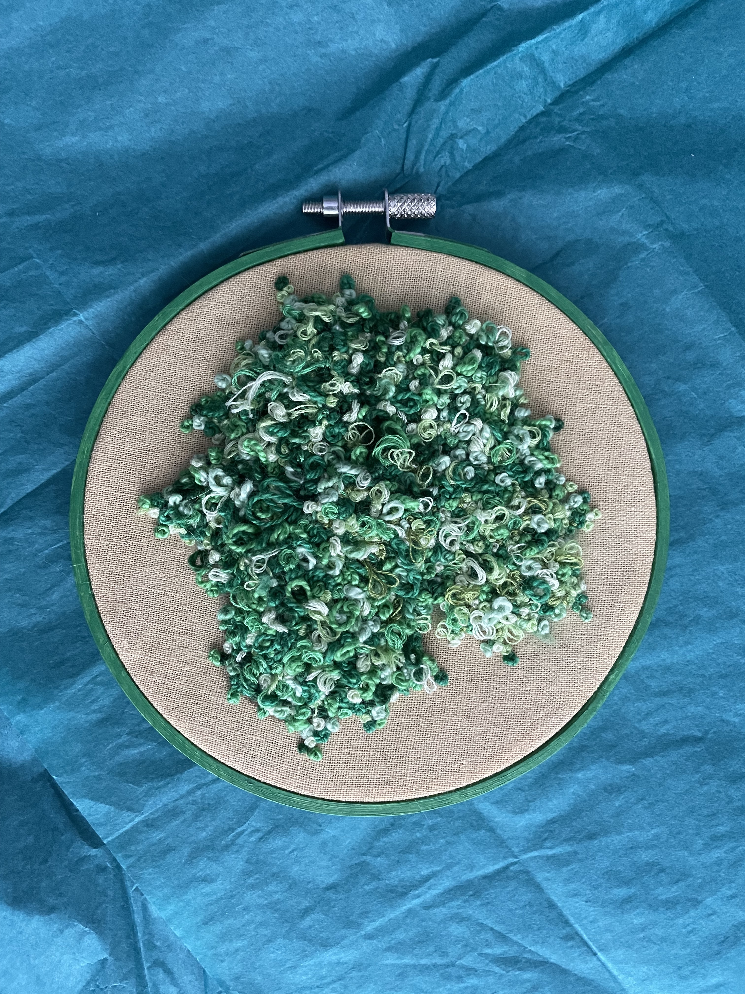 a 5-inch embroidery hoop with green stitched moss on a yellow fabric background